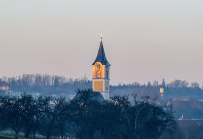 Tower amidst trees and buildings against sky at dusk