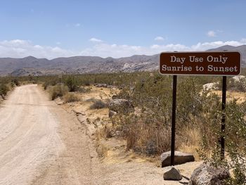 Information sign on road by mountains against sky