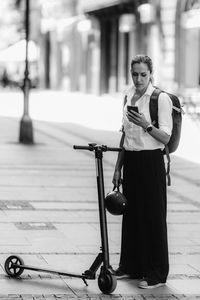 Businesswoman standing and using her smart phone with electric scooter next to her in the city.