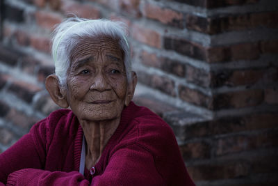 Senior woman looking away against brick wall