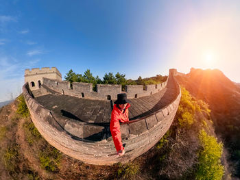 Fish-eye lens of mature man standing on great wall against blue sky