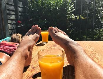 Low section of mid adult man with juice sitting on hardwood floor against plants