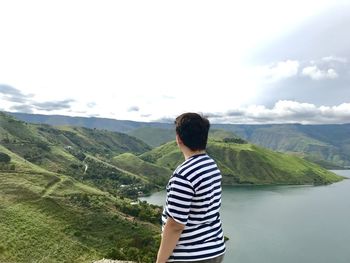 Rear view of man standing on mountain against sky