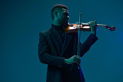 Low angle view of man holding violin against blue background