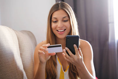 Smiling young woman holding credit card while using mobile phone