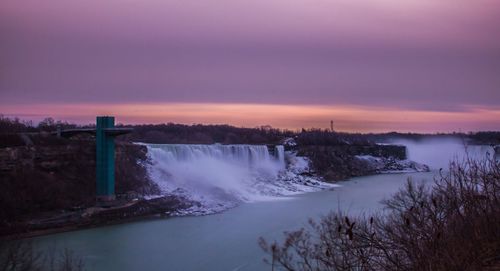 Scenic view of waterfall against cloudy sky at sunrise