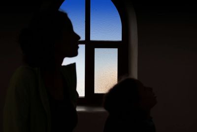 Rear view of silhouette man looking through window