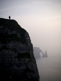 Silhouette person standing on cliff at etretat against sky