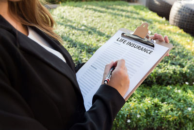 Midsection of female agent with life insurance documents in yard