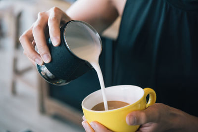 Midsection of woman pouring milk in coffee cup