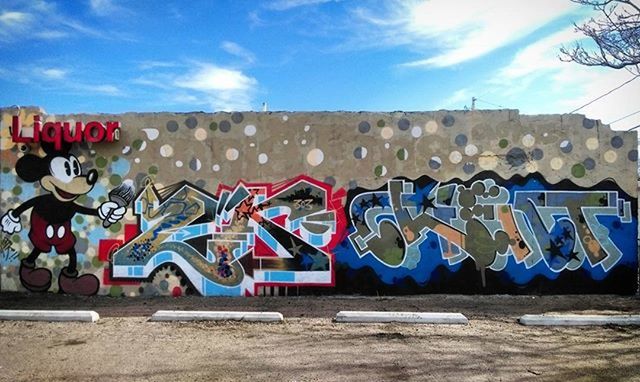 graffiti, text, sky, art, built structure, creativity, architecture, western script, art and craft, building exterior, day, wall - building feature, communication, outdoors, blue, sunlight, cloud - sky, street art, cloud