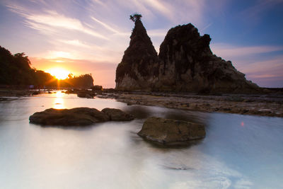 Rocks on shore against sky during sunset