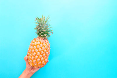 Cropped image of hand holding fruit against blue background