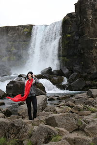 Mid adult woman standing on rocks against waterfall