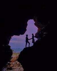 Silhouette people standing on rock formations against sky