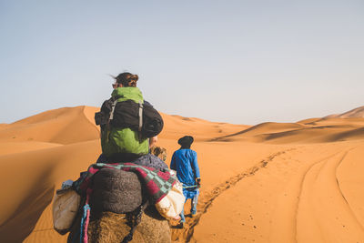 Rear view of man riding horse in desert against sky