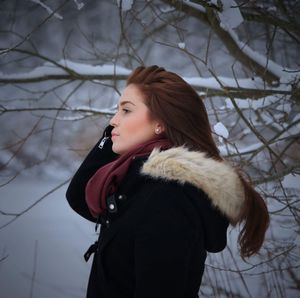 Profile view of young woman standing against branches during winter