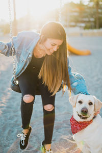 Woman sitting on swing with dog at playground during sunset