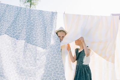 Brother and sister playing in the washing drying on the line in summer