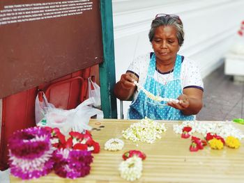 Mature woman making floral garland at market stall