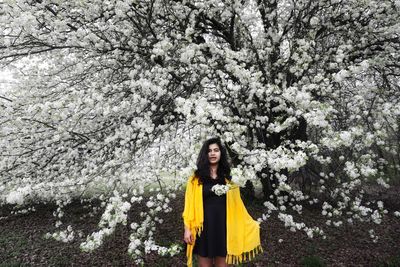 Portrait of young woman standing by flowering tree