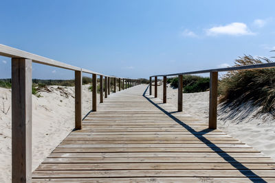 Wooden footbridge leading towards gazebo against sky