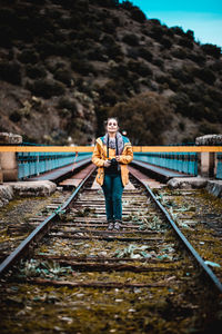 Woman holding camera while standing on railroad track