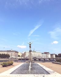 Statue by fountain in city against sky