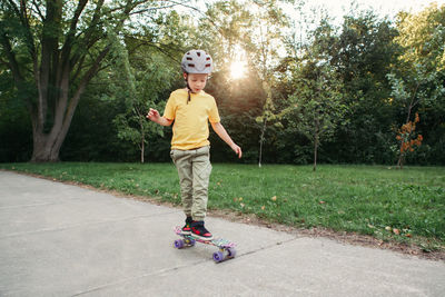 Boy in grey helmet riding skateboard in park on summer day. seasonal outdoor children activity 