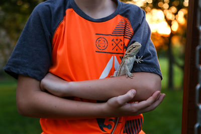 Midsection of boy with bearded dragon standing on field