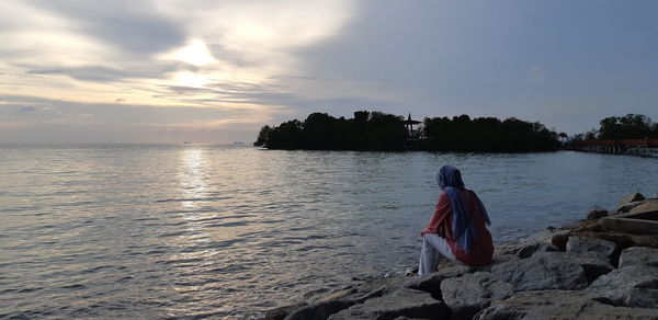 Rear view of man on beach against sky during sunset