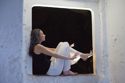 Woman covered with paint sitting on window sill at night