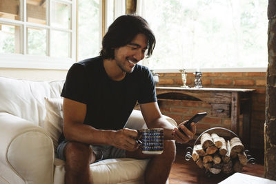 Smiling man using smart phone while sitting on armchair at home