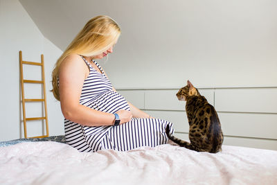 Young pregnant woman sitting on a bed with cat 