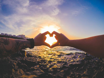 Close-up of hands making heart shape against sky during sunset