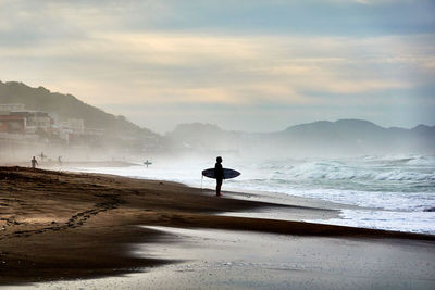 Silhouette man with surfboard on beach against sky during sunrise