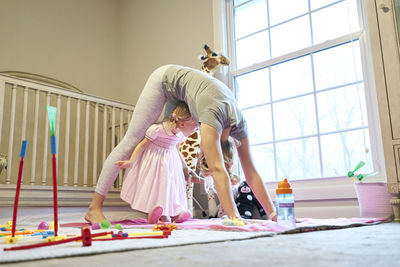 Young mom tries downward dog yoga position with daughter under her