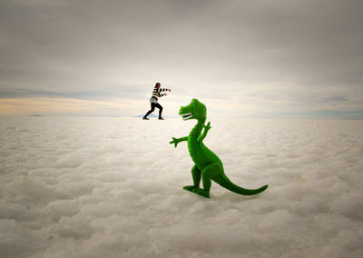 Optical illusion of woman fighting with dinosaur on cloudscape during sunset