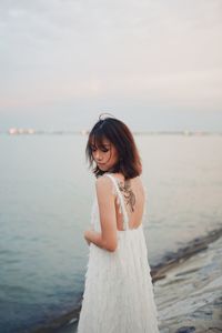 Young woman standing by sea against sky