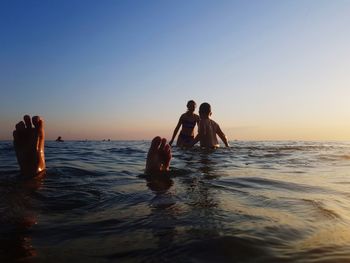 People in sea against sky during sunset