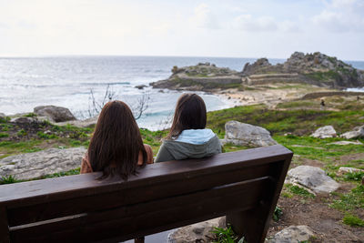 Rear view of women sitting on rock by sea