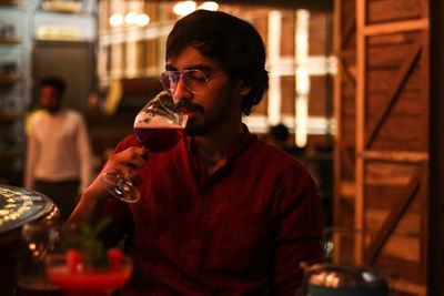 Young man drinking red wine at an indoor restaurant with colorful lights all around him.