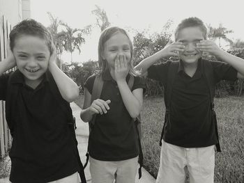 Cheerful children posing as three wise monkeys on footpath