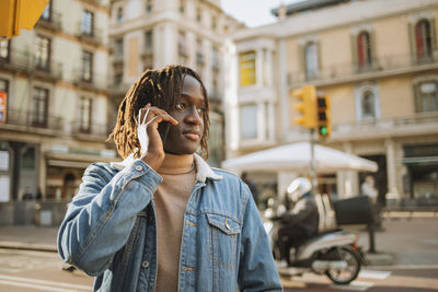 Young man with locs hairstyle talking on phone while looking away in city