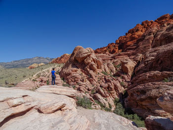 Woman on rock formation against clear blue sky