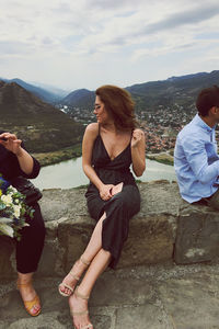 Women sitting on shore against mountains and sky