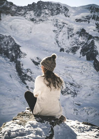 Rear view of woman sitting on cliff during winter