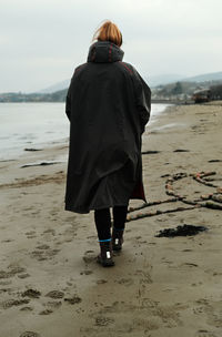 Rear view of woman walking at beach against sky