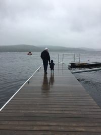 Rear view of father with son standing on pier over sea against sky