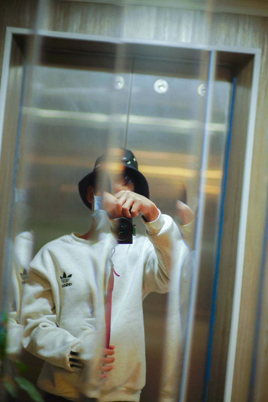 WOMAN PHOTOGRAPHING AT CAMERA WHILE LOOKING THROUGH GLASS